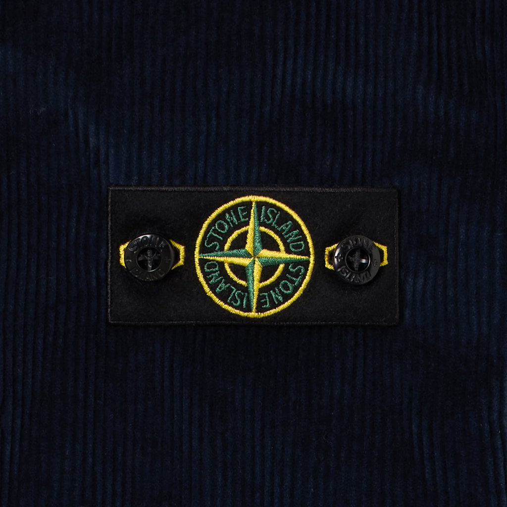 Close-up of a dark navy corduroy fabric with a black rectangular Stone Island logo patch featuring the signature compass logo.