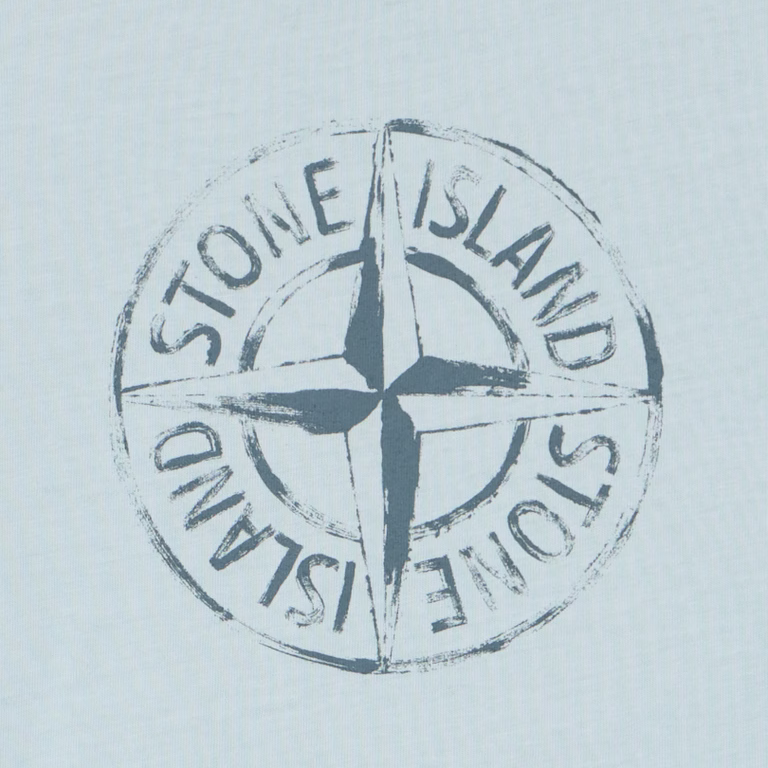A circular Stone Island compass logo printed in a distressed dark blue-gray tone on a very light icy blue fabric background.