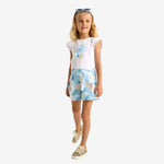 A girl wearing a white t-shirt with a sky rose print and a blue skort.