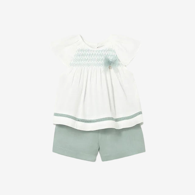 Children's outfit with white top and green shorts on a light gray background