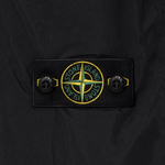 Close-up of a black Stone Island jacket featuring the signature compass badge patch on the chest pocket, flanked by two black buttons.
