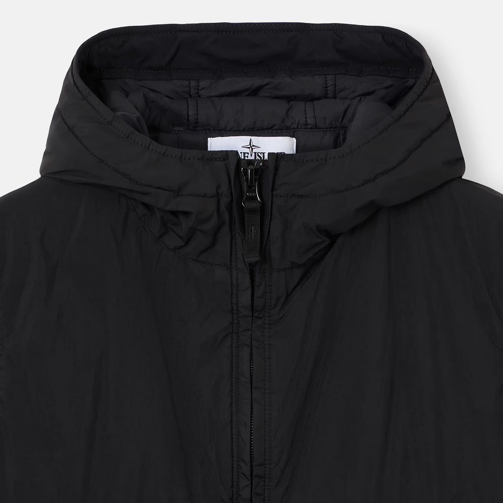 Close-up of a black hooded puffer jacket with a front zipper and a visible Stone Island neck label, shot against a light gray background.