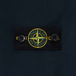 Close-up of a dark navy fabric garment featuring a rectangular black patch with the circular Stone Island compass logo in yellow and green, flanked by two black buttons.