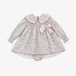A baby girl's long-sleeve dress with a small pink and green floral print, featuring a ruffled Peter Pan collar, smocked bodice, and a matching pink gingham bow on the chest. It is displayed flat on a neutral gray background.