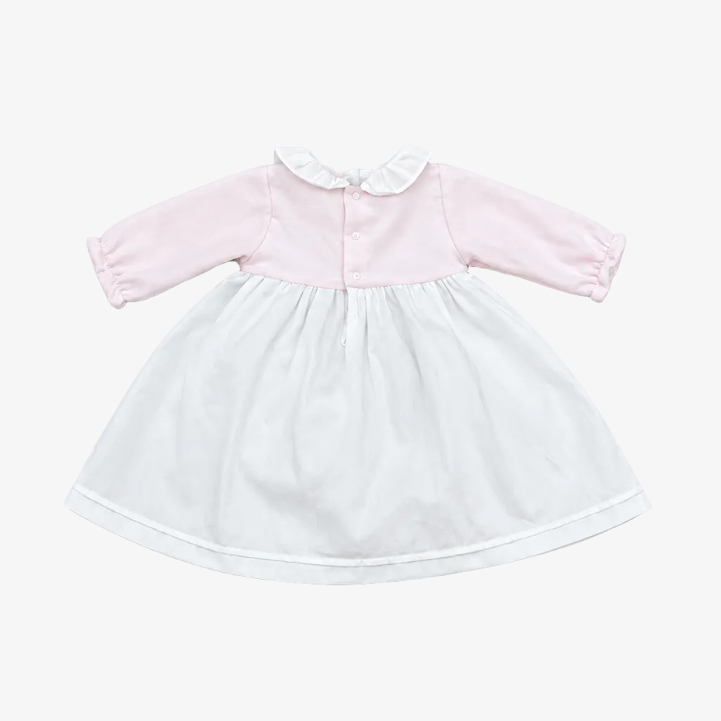 A baby girl's long-sleeve dress with a light pink bodice, white ruffled collar, and a white flared skirt, laid flat on a neutral gray background.