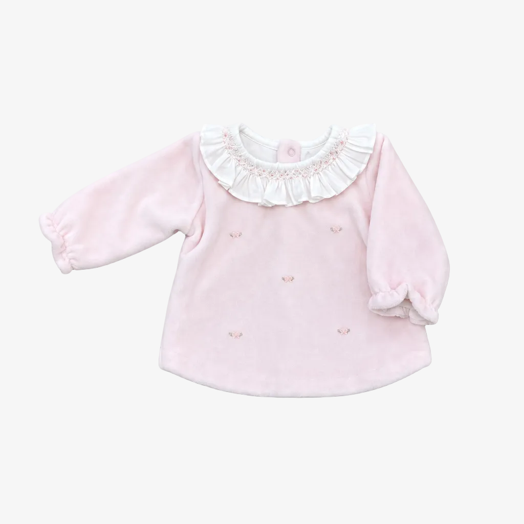 A pink long-sleeve baby top with a white ruffled collar and small embroidered details, laid flat on a neutral gray background.