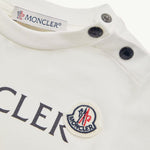 Close-up of a white Moncler garment showing the inner neck label, snap closures, and part of the chest logo with the circular Moncler emblem.