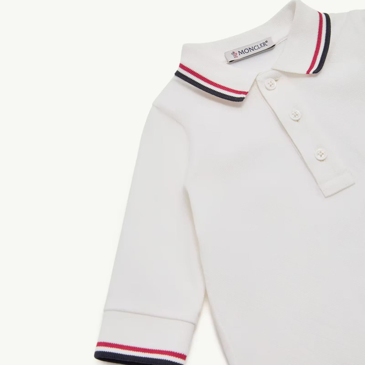 A close-up of a white long-sleeve polo shirt by Moncler, featuring the brand's signature red, white, and navy blue striped knit collar and matching striped cuffs.