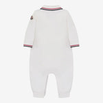 White long-sleeve baby jumpsuit shown from the back, featuring a striped collar and cuffs in navy, red, and white, with a small embroidered logo patch on the upper left shoulder.