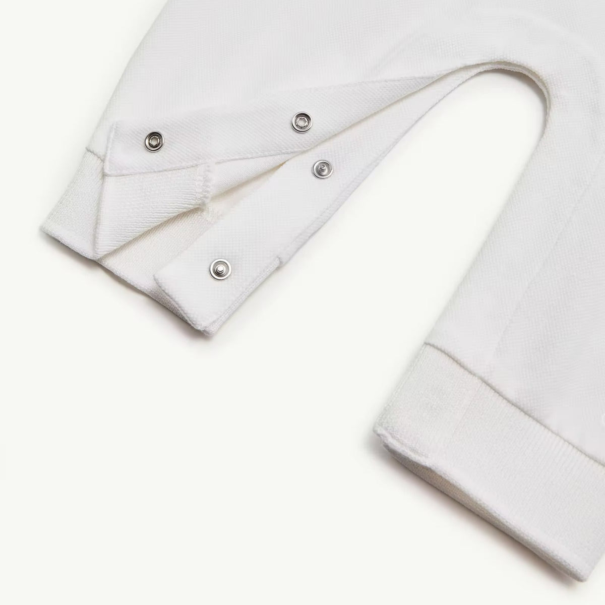 Close-up of a white garment sleeve with three silver metal snap buttons on the cuff, shown on a plain white background.