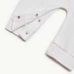 Close-up of a white garment sleeve with three silver metal snap buttons on the cuff, shown on a plain white background.