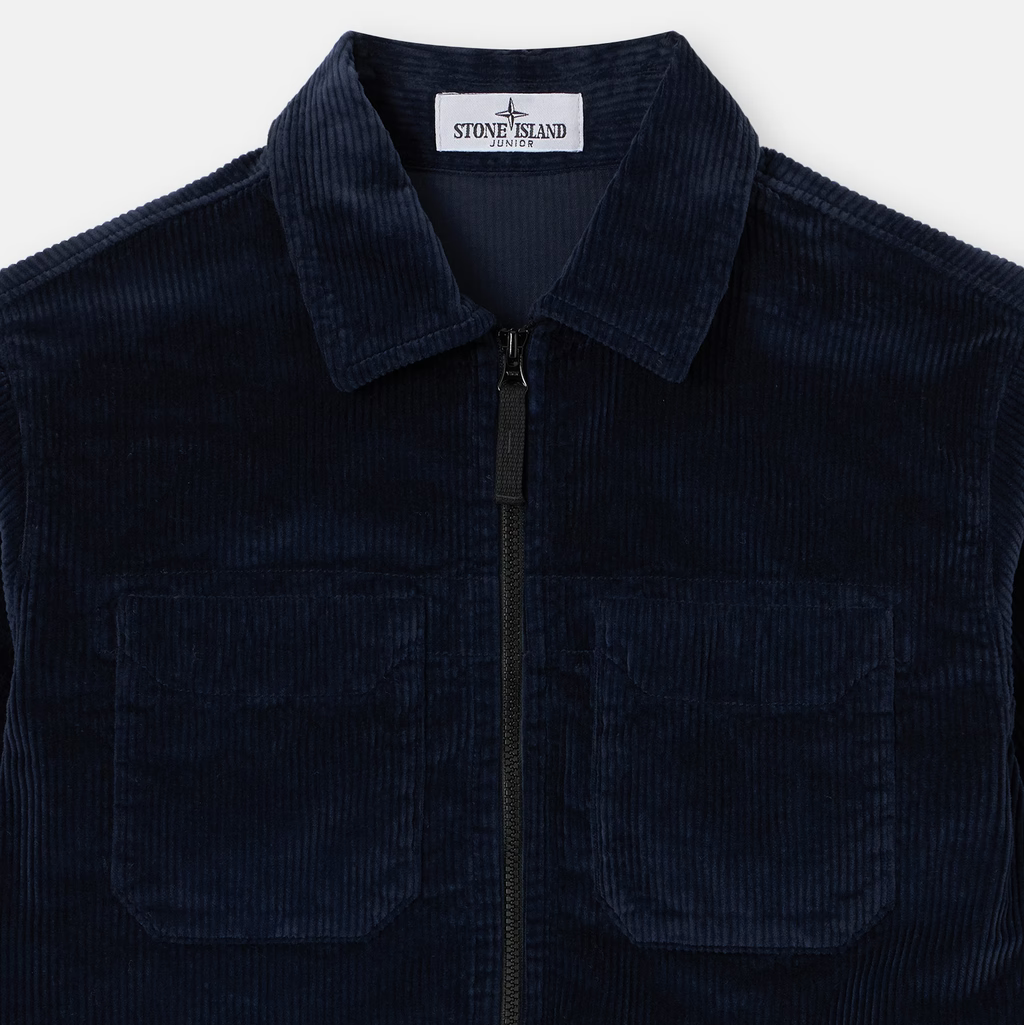 A close-up of a dark navy blue corduroy zip-up jacket by Stone Island, featuring a collar, a front zipper, and two chest pockets, set against a light gray background.