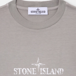 Close-up of a Stone Island Junior t-shirt in a light gray heather color, featuring a white printed compass rose and 'STONE ISLAND' text on the chest, with the brand label visible inside the collar.