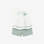 Children's outfit with white top and green shorts on a light gray background