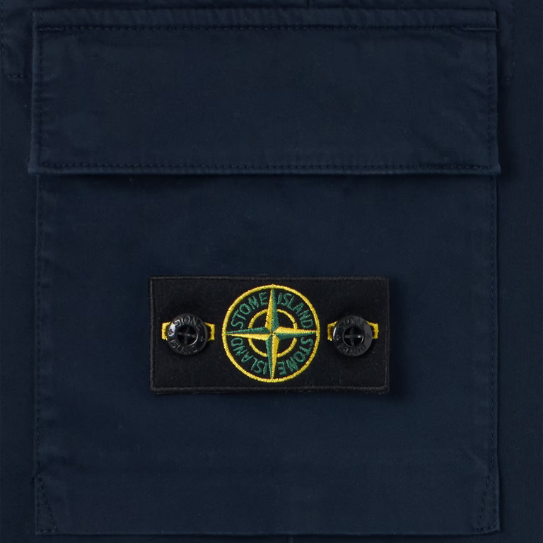 Close-up of a dark navy blue fabric pocket with a rectangular Stone Island logo patch on the front, featuring the brand's compass logo in yellow, green, and black.