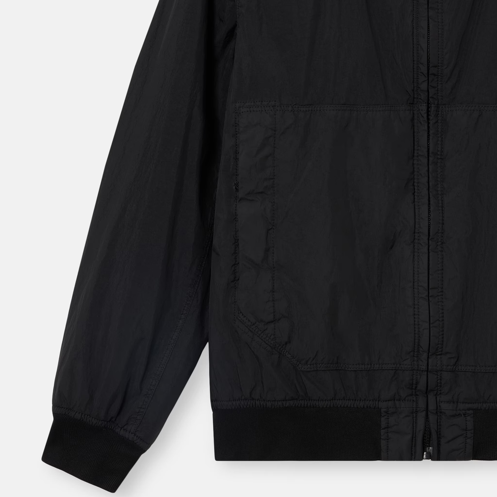 Close-up of a black lightweight jacket with a front zipper, long sleeve, and ribbed cuffs and hem, shown on a light gray background.