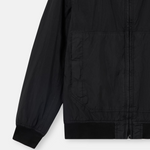 Close-up of a black lightweight jacket with a front zipper, long sleeve, and ribbed cuffs and hem, shown on a light gray background.