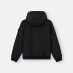 A black hooded jacket shown from the back, featuring a subtle vertical texture and a small black rectangular patch on the left sleeve, set against a light gray background.