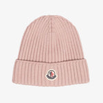 A light pink ribbed knit beanie hat featuring a folded cuff with a circular embroidered Moncler logo patch, set against a solid light gray background.