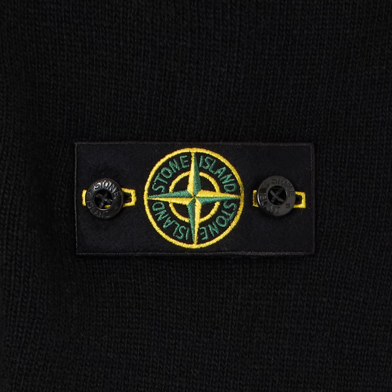 Close-up of a black knit garment featuring a rectangular black label with the circular Stone Island compass logo in yellow and green, flanked by two black buttons.