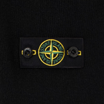 Close-up of a black knit garment featuring a rectangular black label with the circular Stone Island compass logo in yellow and green, flanked by two black buttons.