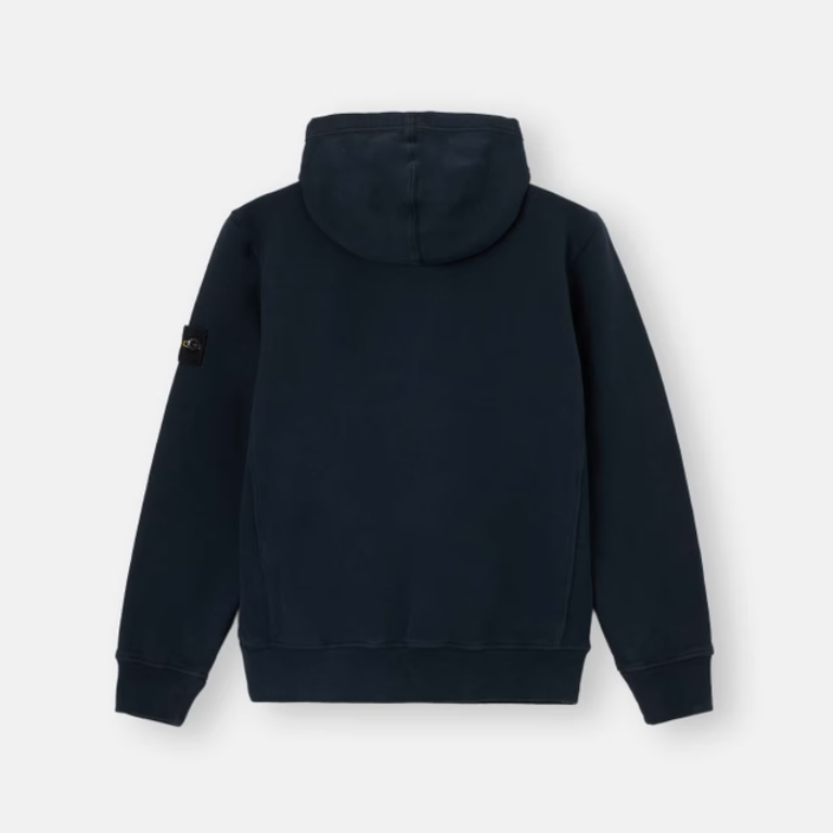 A dark navy blue hooded sweatshirt shown from the back, featuring a small black brand patch on the left sleeve, set against a plain light gray background.