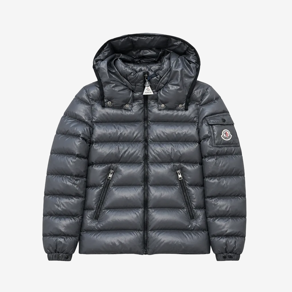 A dark gray puffer jacket with a hood, shown flat against a light gray background. The jacket features horizontal quilting, two zippered pockets on the front, and the iconic circular Moncler logo patch on the left sleeve.