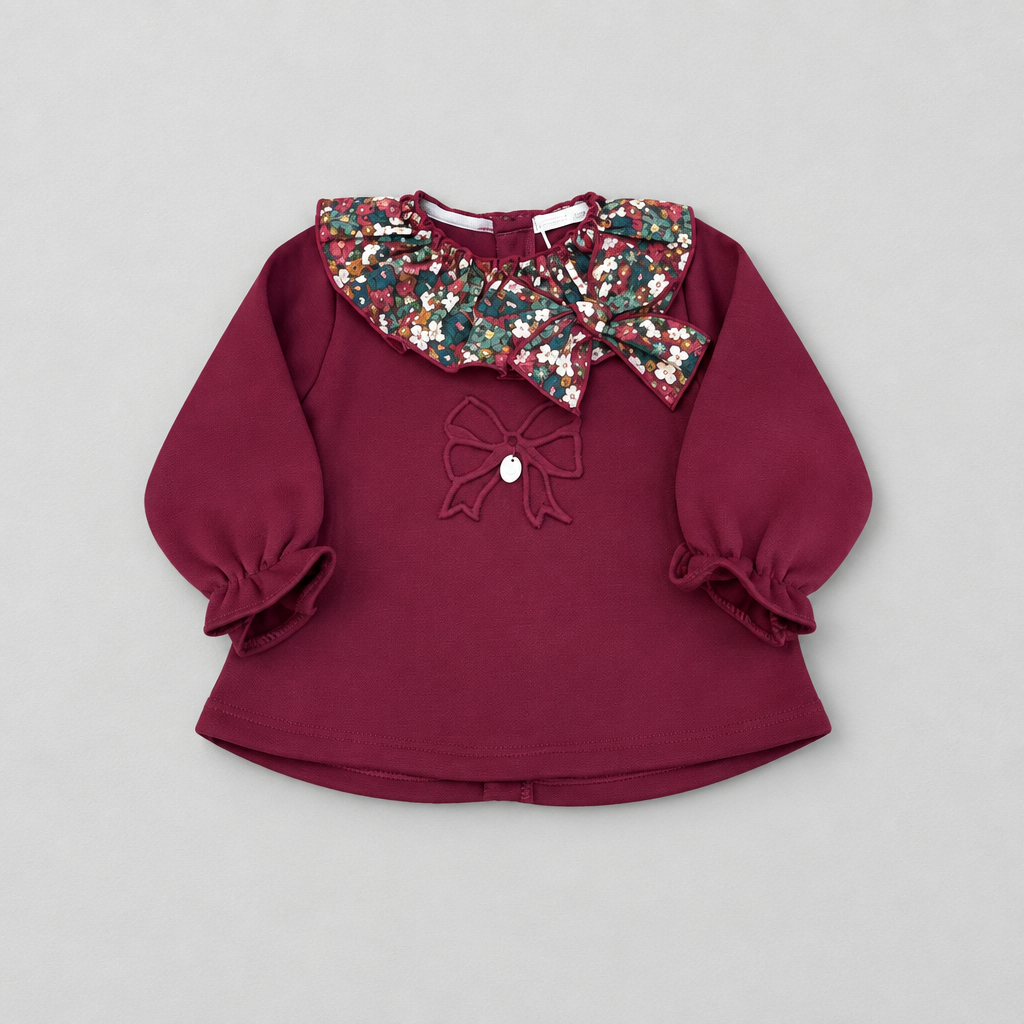 A toddler girl's long-sleeve top in deep burgundy, featuring a large floral-patterned ruffled collar with sequins, a matching embroidered bow on the chest, and ruffled cuffs.