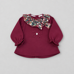 A toddler girl's long-sleeve top in deep burgundy, featuring a large floral-patterned ruffled collar with sequins, a matching embroidered bow on the chest, and ruffled cuffs.