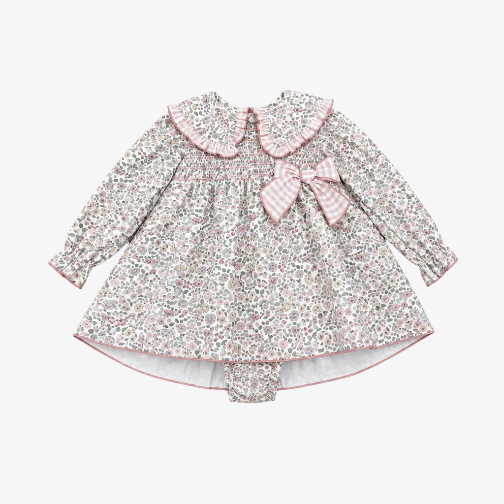 A baby girl's long-sleeve dress with a small pink and green floral print, featuring a ruffled Peter Pan collar, smocked bodice, and a matching pink gingham bow on the chest. It is displayed flat on a neutral gray background.