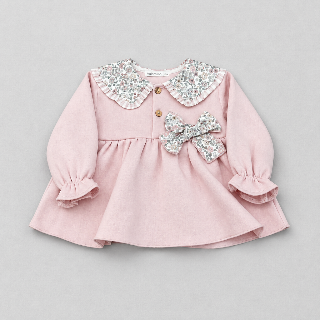 A baby girl's long-sleeve pink dress with a ruffled floral-patterned Peter Pan collar, two gold buttons, and a matching bow on the chest, shown on a neutral gray background.