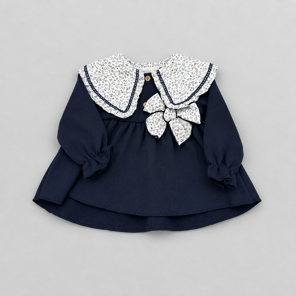 A navy blue long-sleeve baby dress with a large white floral-patterned Peter Pan collar, a matching bow at the center, and ruffled cuffs, laid flat on a light gray background.