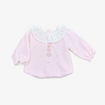 A baby long-sleeve top in light pink fleece, featuring a white ruffled collar with small embroidered details and a small ballerina embroidery on the chest, laid flat on a neutral gray background.
