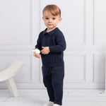 A baby boy wearing a navy blue knitted sweater and trousers set, standing against a white background. 