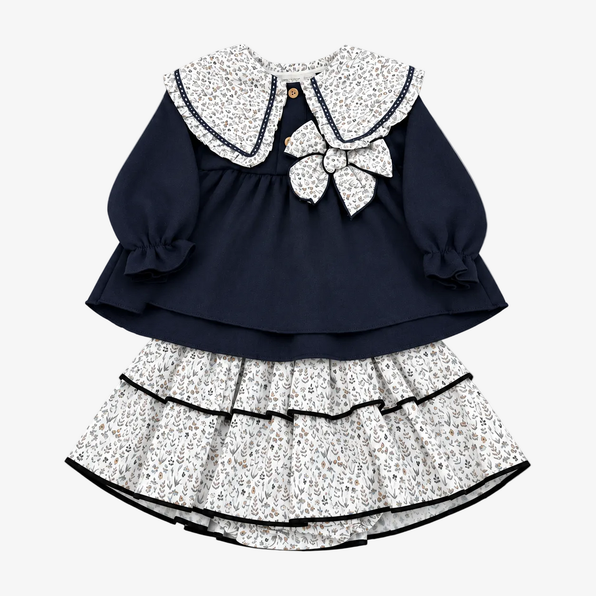 A two-piece toddler girl's dress set featuring a navy blue long-sleeve top with a white floral-patterned Peter Pan collar and bow, paired with a matching ruffled skirt, laid flat on a neutral gray background.