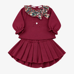 A toddler girl's two-piece outfit featuring a long-sleeve top and pleated skirt in deep burgundy. The top has a large, decorative multi-colored sequin Peter Pan collar, a matching sequin bow on the chest, and ruffled cuffs.