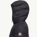 A close-up side view of a black Moncler puffer jacket with the brand's circular logo patch visible on the upper sleeve, set against a plain off-white background.