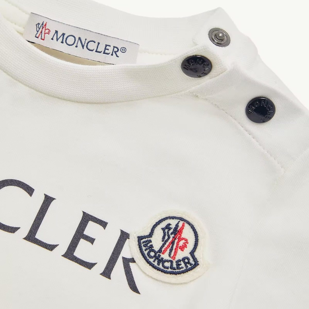 Close-up of a white Moncler garment showing the inner neck label, snap closures, and part of the chest logo with the circular Moncler emblem.